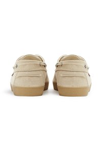Scarpe in tela beige con una texture morbida, punta rotonda e suola in gomma marrone chiaro. Presentano due fori su ogni lato per i lacci.