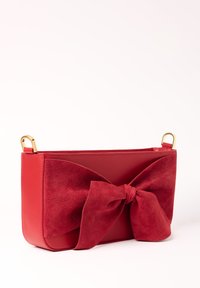 Borsa a mano in pelle rossa con un grande fiocco in suede, texture liscia, forma rettangolare, anelli in oro e design aperto.
