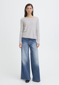 Maglione grigio chiaro con puntini in rilievo, scollo rotondo, abbinato a jeans denim blu a gamba larga con lavaggio sbiadito e vestibilità classica.