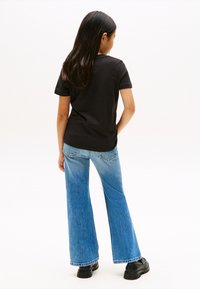 T-shirt en coton noir associé à un jean évasé bleu. Le jean présente une teinte délavée et la tenue est complétée par des chaussures noires.
