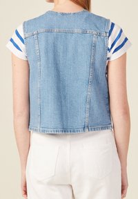 Kamizelka dżinsowa, w jasnoniebieskim odcieniu, bez rękawów, krótki fason. Posiada szwy z tyłu i czysty brzeg. Połączona z koszulą w paski i białymi spodniami.