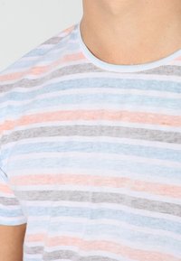 T-shirt à manches courtes rayé dans des teintes de bleu, gris et corail avec un col rond ; fabriqué en coton léger avec une texture légèrement décolorée.