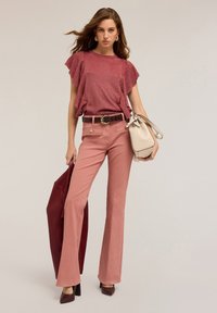 Pantalones acampanados de color rosa empolvado con una blusa texturizada a juego que cuenta con mangas con volantes. Los accesorios incluyen un cinturón marrón y un bolso crema.