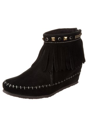 Bottine en daim noir avec surpiqûres blanches, détail à franges autour du col et clous décoratifs dorés et noirs sur un talon compensé.