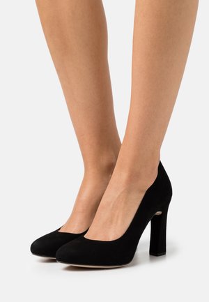 Schwarze Wildleder-Pumps mit runder Zehe und Blockabsatz, die eine glatte Textur und eine Aussparung an den Seiten präsentieren.