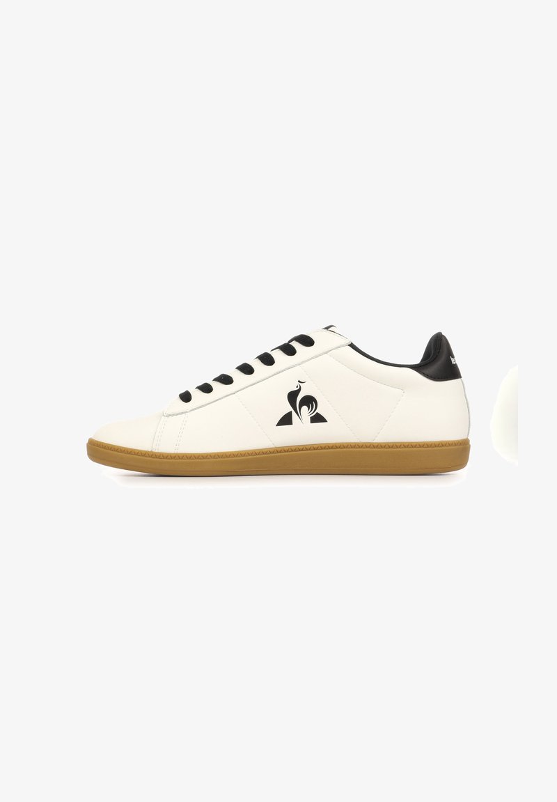 Baskets basses blanches avec lacets noirs, détail talon noir, semelle marron et logo coq noir sur le côté.