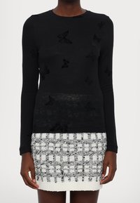 Haut noir à manches longues orné d'applicatifs papillon en velours, associé à une minijupe texturée blanche et noire avec un motif en quadrillage.