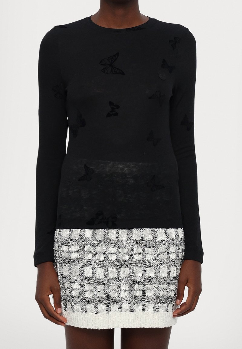 Haut noir à manches longues orné d'applicatifs papillon en velours, associé à une minijupe texturée blanche et noire avec un motif en quadrillage.