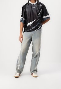 Musta ja harmaa urheilupaita salamakuviolla ja valkoisilla raitoja, yhdistettynä haalistuneisiin sinisiin farkkuihin, joissa on kolme pystysuoraa valkoista raitaa.