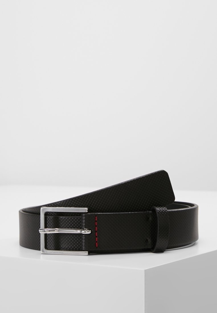 Ceinture en cuir texturé noir avec boucle rectangulaire argentée et détail de surpiqûre rouge, présentée enroulée sur une surface blanche.