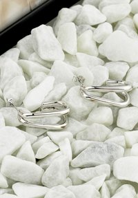 Silverörhängen i hoops med en vriden design och en slät, reflekterande yta, placerade bland vita dekorationsstenar.