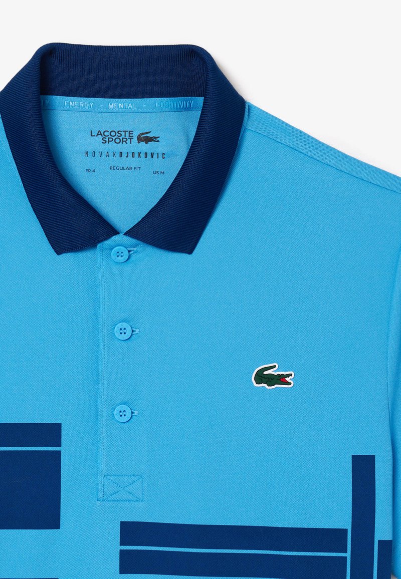 T-shirt polo bleu avec col marine, trois boutons et logo crocodile Lacoste. Présente des rayures horizontales marines sur la poitrine. Coupe classique.