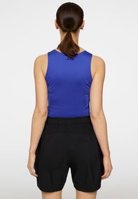 Blå ärmlös topp med hög halsringning, kombinerad med lösa svarta shorts med elastisk midja. Enkelt mönster, enfärgade.