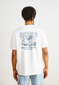 White cotton t-shirt featuring blue graphic print on the back, with the text "DICKIES PROTECTIVE UNIFORMS QUALITY MADE" and a figure.