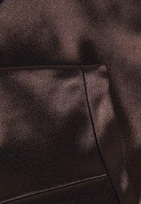 Tissu en satin brun foncé lisse avec une texture de tissage fin visible et une couture apparente créant un bord plié.