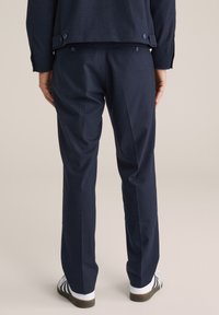 Marinblå randiga kostymbyxor med skräddarsydd passform, med sidofickor och knappelement vid midjan. Kombineras med vita skor.