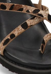 Sandalia de tiras manchada en marrón y negro con una plantilla negra suave y suela texturizada. Presenta un material suave, similar al de piel de animal, en las tiras.