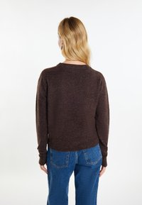 Brązowy sweter dzianinowy z długimi rękawami, okrągłym dekoltem i luźnym krojem. Połączony z niebieskimi jeansami z wysokim stanem z tylnymi kieszeniami.