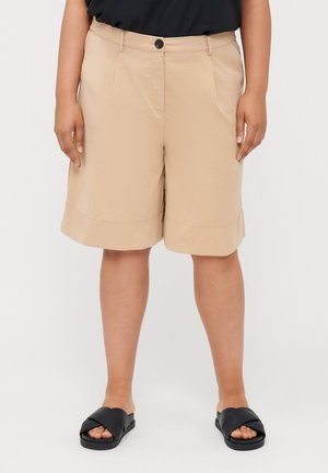 Beige shorts with a relaxed fit, featuring front pockets, a button closure, and a rolled hem. Worn with black slide sandals.