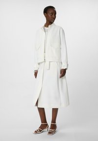 White zip-front bomber jacket with two front pockets, paired with a matching white floor-length skirt featuring a front slit and minimalist design.