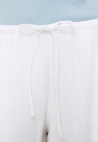 Λινή λευκή παντελόνα με ζωνάκι που δένει στη μέση, με λεία υφή και μινιμαλιστικό σχεδιασμό. Συνδυασμένη με φωτεινό γαλάζιο πλεκτό ριμπ τοπ.