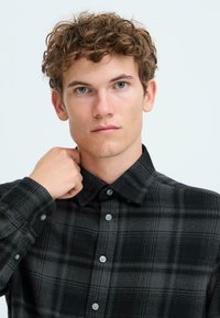 Black and gray plaid shirt with a button-down collar, long sleeves, and multi-tone check pattern. Fabric appears soft and textured.