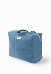 Sac fourre-tout en denim bleu de forme rectangulaire, avec une fermeture éclair dorée et deux poignées. Il possède une étiquette à l'avant. Texture lisse, matériau robuste.