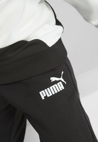 Schwarze Sweatpants mit einem gerippten Bund, der ein auffälliges weißes Puma-Logo am linken Oberschenkel trägt. Hergestellt aus einem weichen, strukturierten Stoff.