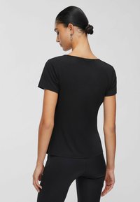 Schwarzes T-Shirt mit kurzen Ärmeln und rundem Ausschnitt, aus glattem Stoff, figurbetontem Schnitt und einem leicht geschwungenen Saum im Rückenbereich.