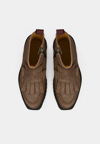 Chaussures en daim marron avec un design à franges, un bout rond, des zips latéraux et une semelle en caoutchouc noire. L'intérieur est jaune.