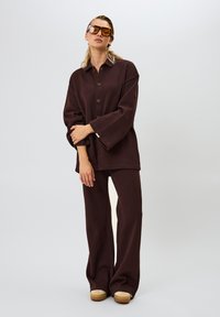 Bruine corduroy oversized button-up shirt en bijpassende wijde broek, met een textuur oppervlak en gecombineerd met tan schoenen en bruine zonnebril.
