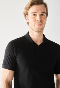Sort polo shirt med klassisk krave, korte ærmer og knaplukning. Stoffet er glat med en subtil tekstur.