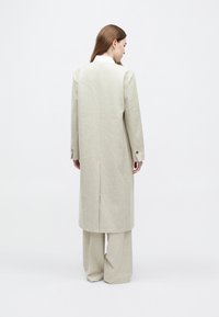 Jasnoszary wełniany płaszcz o dopasowanym kroju, z długimi rękawami i rozcięciem z tyłu, zestawiony z pasującymi szerokimi spodniami.