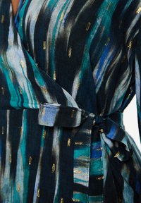 Vestido tipo wrap en un azul marino oscuro con franjas en verde azulado y azul, acentuado con detalles dorados. Presenta una cintura atada y una textura de tejido suave.