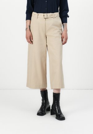 Beige wijde broek met een hoge taille en riem, voorzien van een soepele textuur. Gepaard met zwarte enkellaarsjes, benadrukt het ontwerp de relaxte pasvorm.
