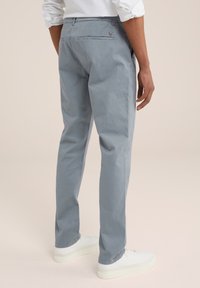 Pantaloni in cotone azzurro chiaro con vestibilità slim, dotati di una tasca sul retro con chiusura a bottone e una texture liscia, abbinati a sneakers bianche.
