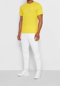 Yellow cotton T-shirt with crew neck and small white Nike logo; paired with white joggers and white athletic shoes.