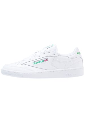 Zapatilla blanca Reebok de corte bajo con logotipo verde y bandera del Reino Unido en el lateral, cierre de cordones y suela de goma.