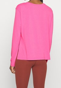 Lätt, långärmad t-shirt i klar rosa, med rund halsringning och sidofickor, kombinerad med bruna leggings. Enkelt, avslappnat design.