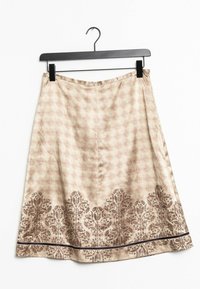 Et knælængde A-formet skørt i et lysebeige stof med et blomstret brunt mønster langs kanten og en kontrasterende sort kant.