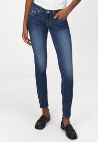 Jeans in denim blu scuro slim fit con vita media, dotati di tasche anteriori e chiusura con bottone. Indossati con mocassini neri.