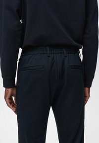 Pantalons de jogging noirs en tissu texturé, dotés d'une taille élastique, de deux poches arrière et d'un design de coupe décontractée.