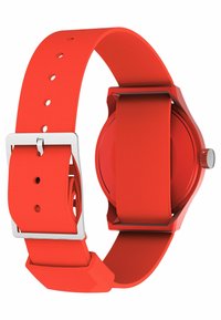 Montre en silicone rouge avec une texture lisse, un boîtier rond et des éléments en métal argenté. Dispose d'une fermeture à boucle et d'un design élégant et minimaliste.