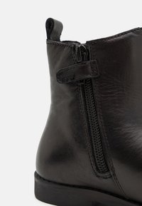 Bottine en cuir noir avec fermeture éclair latérale, texture lisse, bout arrondi et design minimaliste avec un petit talon.