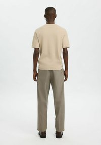 Bežinė trumpa rankovė marškiniai ir šviesiai pilki kelnės, su laisvu pajautimu ir lygiu tekstūru, matomi iš nugaros ant neutralios fono.