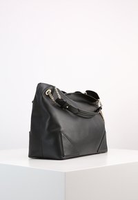 Black leather handbag with a structured design, chain accents, and triangular detailing on the sides. Smooth texture, spacious silhouette.