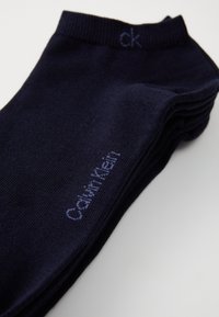 Tamno plave čarape od mekog materijala, sa rebrastim rubom, sa izvezenim logotipom "Calvin Klein" u svijetloplavoj boji blizu članka.