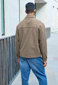 Brun, struktureret jakke med krave, rygpanel og knapmanchetter, paired med lyseblå, løstsiddende denimjeans.