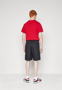 Red short-sleeve t-shirt, black elastic waist shorts, white Nike logo, white socks, and black/red sneakers, viewed from the back.