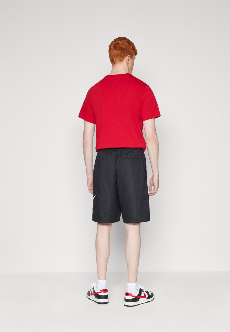 Rotes Kurzarm-T-Shirt, schwarze Shorts mit elastischem Bund, weißes Nike-Logo, weiße Socken und schwarz-rote Sneakers, von hinten betrachtet.